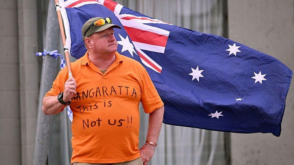 Woman wearing orange t‑shirt waving the Australian flag