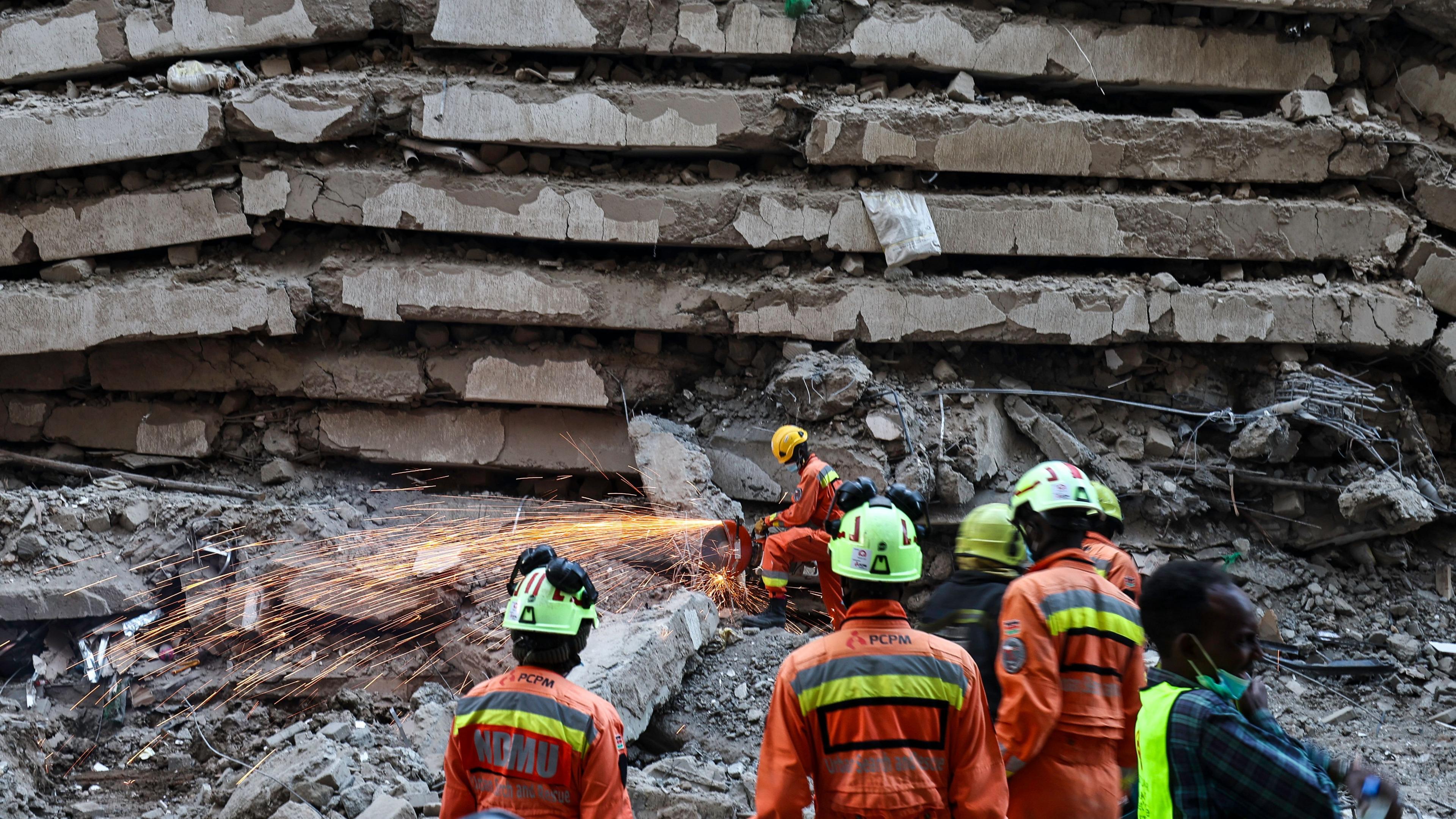 An emergency worker saws through metal and concrete as others watch at a building collapse in Nairobi.
