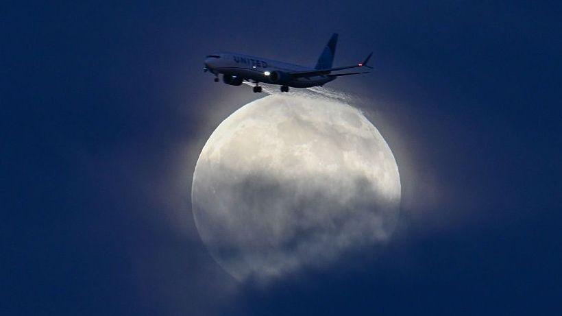 Glowing white moon rising over blue clouds with a plane in the foreground